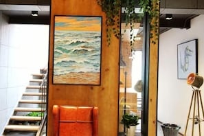 A staircase with a wooden handrail, a painting of a seascape, and a tripod lamp. - In Hotels (Qingdao)