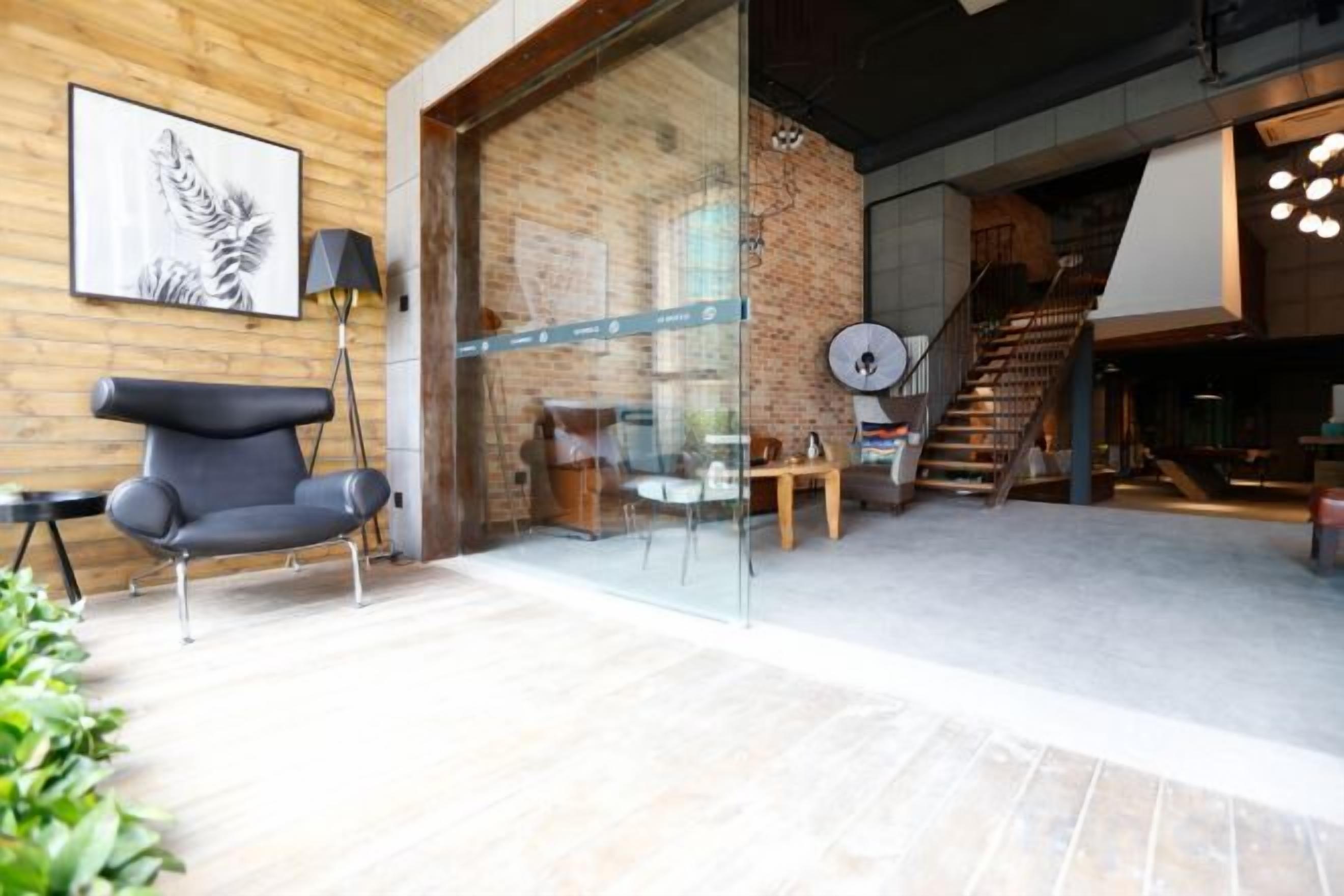 Un interior moderno con una pared de ladrillo, una puerta de cristal que da a una escalera y una zona de estar con una silla y una mesa.
