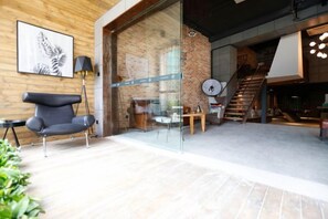 A modern interior with a brick wall, a glass door leading to a staircase, and a seating area with a chair and a table. - In Hotels (Qingdao)