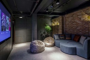 A modern lounge area with a curved sofa, two bean bags, and a large screen displaying images. - In Hotels (Qingdao)