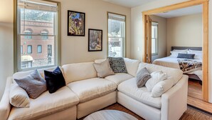 A modern living room with a sectional sofa, a bed, and large windows offering a view of a building. - Walk to Hot Springs: Updated Retreat in Dtwn Ouray (Ouray)