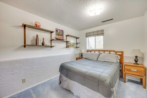 Une chambre à coucher comprenant un lit, des tables de chevet en bois, une fenêtre avec des stores et des étagères murales ornées d’objets décoratifs.