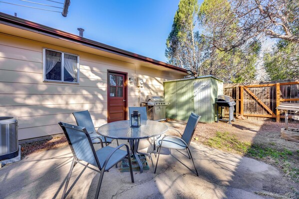 Une terrasse avec une table ronde et des chaises, un barbecue et un abri de jardin.