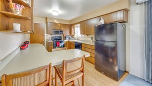 A modern kitchen with wooden cabinets, a stainless steel refrigerator, a microwave, and a dishwasher. There is a dining table with two chairs. - 2 Mi to Citadel Mall: Home w/ Furnished Patio! (Colorado Springs)