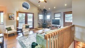 A spacious living room with a stone fireplace, wooden flooring, and a ceiling fan. - Deck + Mountain Views: Fairplay Family Escape! (Fairplay)