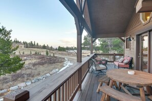 Une terrasse en bois avec des meubles d’extérieur, une vue sur un paysage naturel et un bâtiment doté d’une grande fenêtre.
