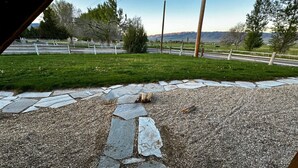 A stone pathway leading to a grassy area with a fence and mountains in the background. - Cabin 10 Deluxe Lrg 2 Story at the Almo Inn near City of Rocks/Castle Rock Idaho (Almo)