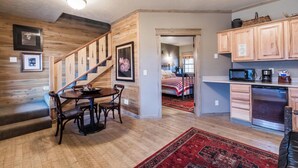 A cozy interior with a wooden staircase, a dining area with a table and chairs, a kitchen with wooden cabinets and appliances, and a hallway leading to a bedroom. - Cabin 10 Deluxe Lrg 2 Story at the Almo Inn near City of Rocks/Castle Rock Idaho (Almo)