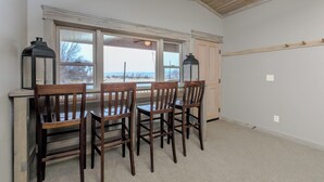 A dining area with a table and four chairs, large windows, and two wall-mounted lanterns. - Cabin 10 Deluxe Lrg 2 Story at the Almo Inn near City of Rocks/Castle Rock Idaho (Almo)