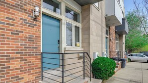 Un edificio residencial con puerta azul, fachada de ladrillo y un pequeño balcón con barandilla metálica.