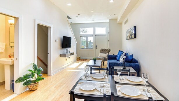 Una sala de estar moderna con comedor listo para seis personas, un sofá, un televisor y una escalera que lleva a otra habitación.