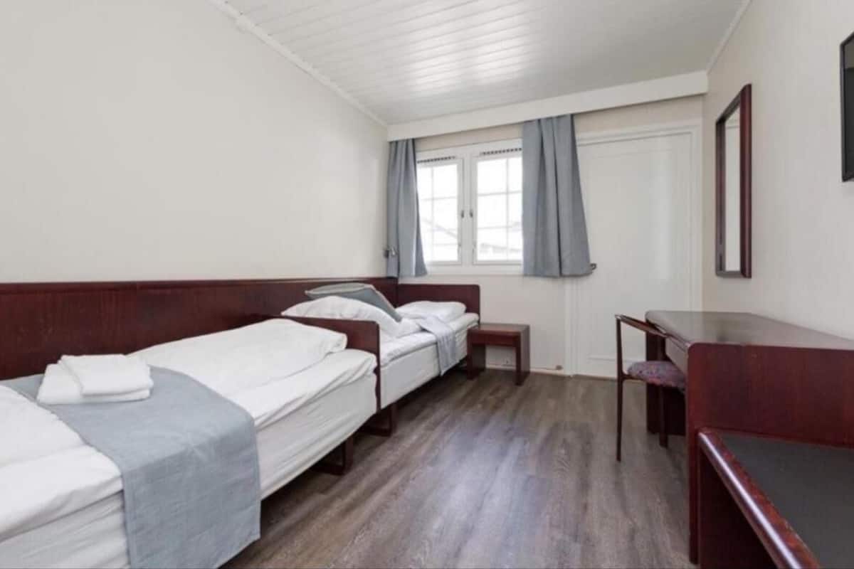 A hotel room with two single beds, a small desk, and a chair.