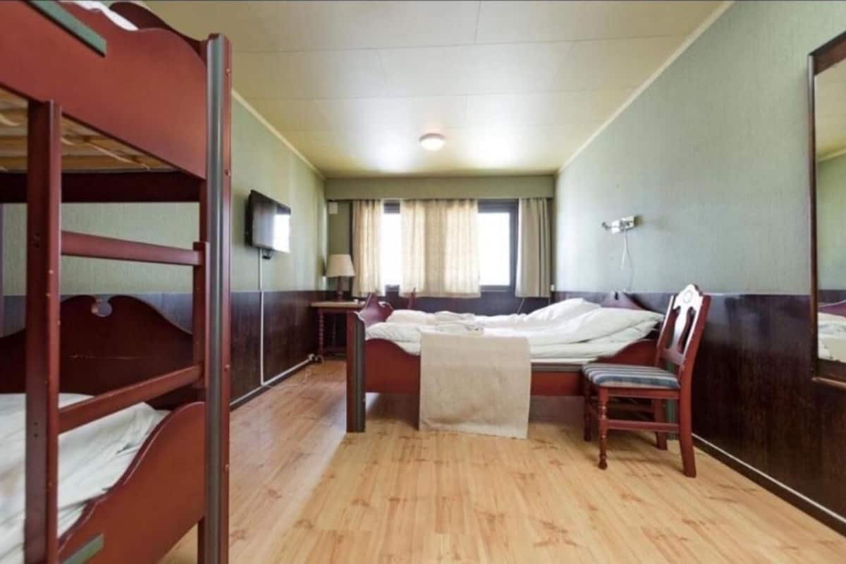 A room with bunk beds, a single bed, a chair, a desk, and a television.