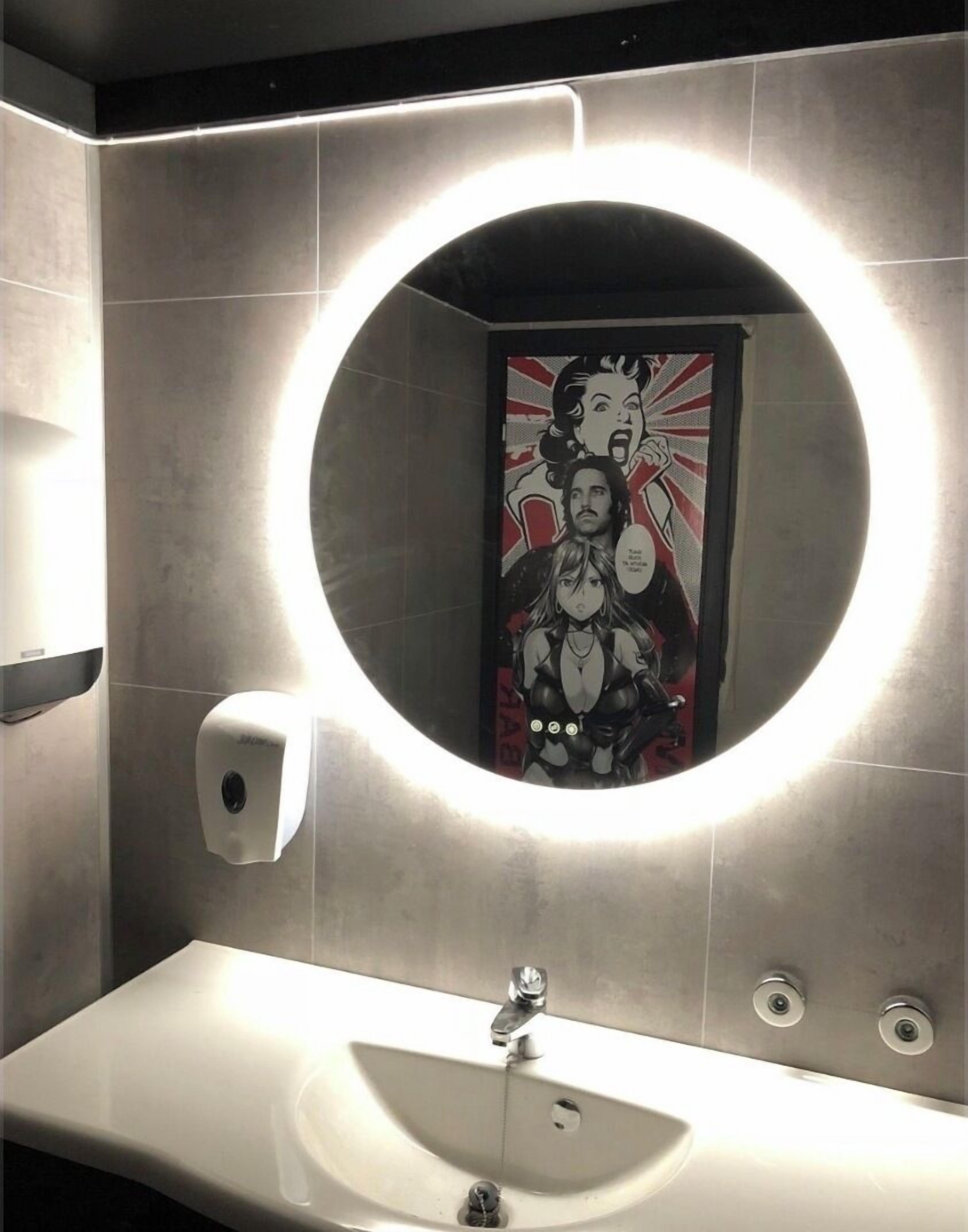 Un bany modern amb un mirall rodó, un assecagats mans i un lavabo.