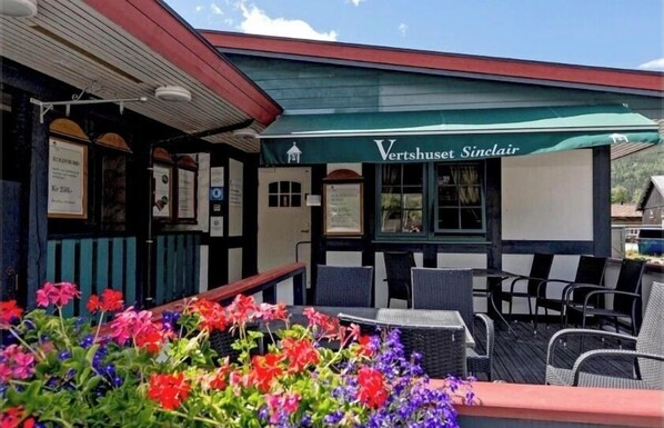 An outdoor seating area with wicker furniture and a green awning labeled 'Vertshauset Sinclair.' - Jafs Sinclair (Kvam)