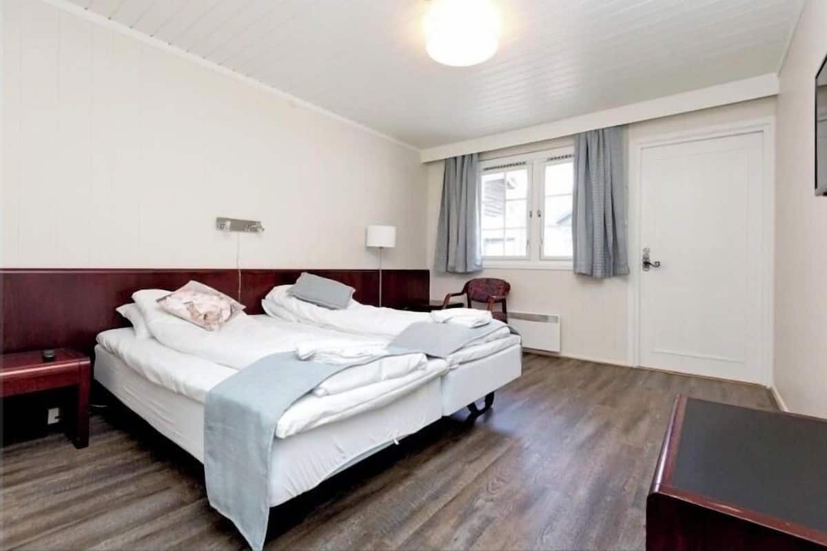 A single bed with a headboard, a bedside table, a lamp, and a window with curtains.