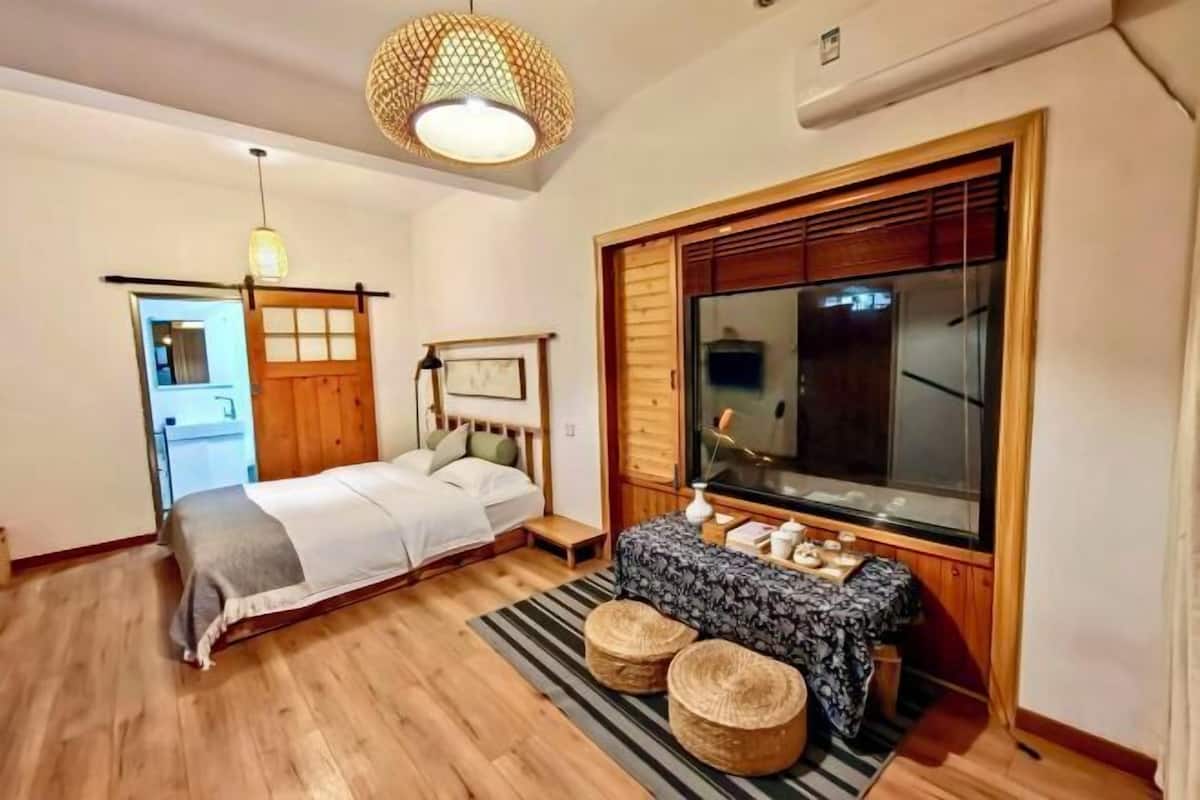 A bedroom with a bed, bedside table, and a large window.