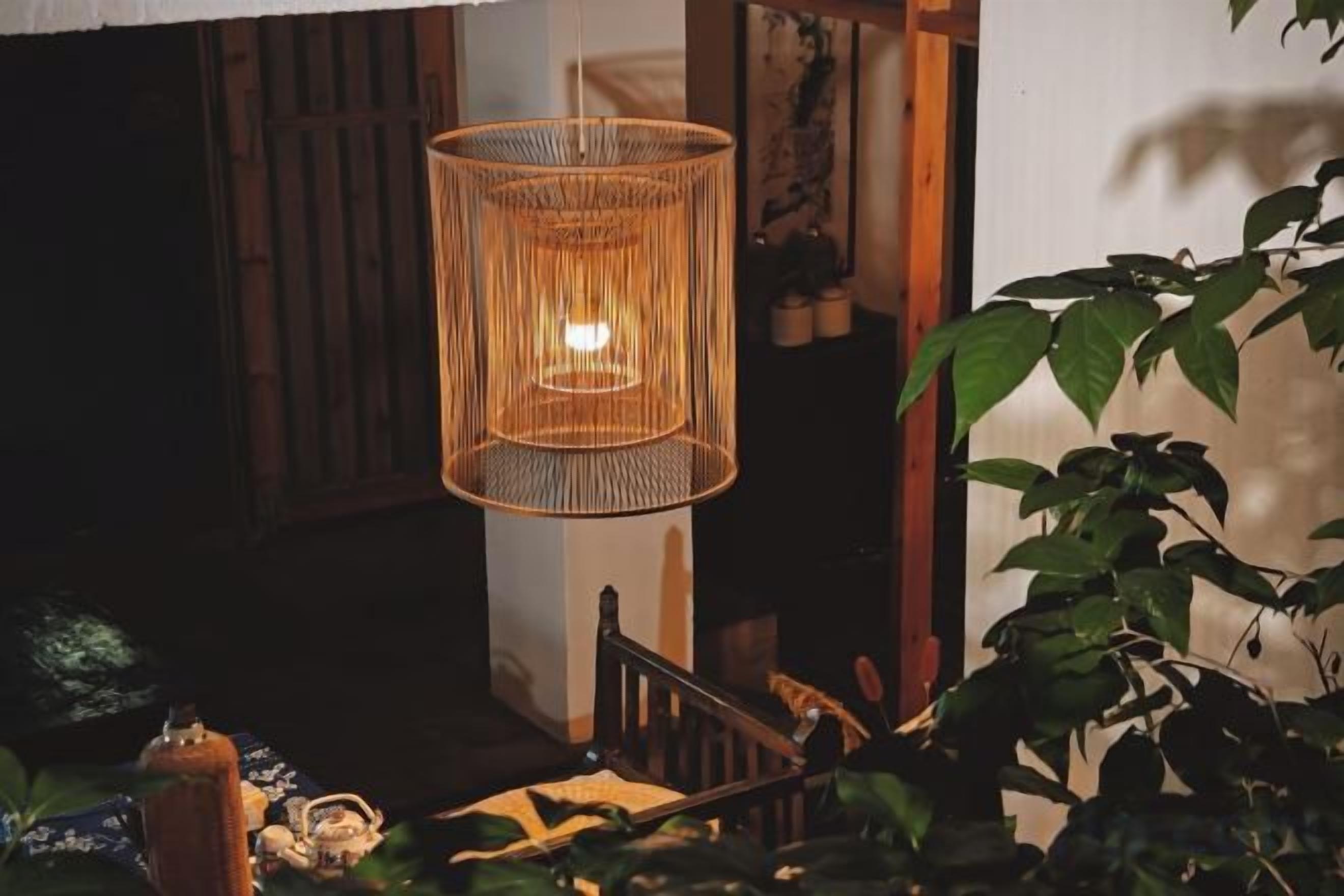 A wicker hanging light fixture in a room with a wooden chair and a potted plant.