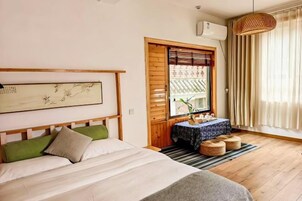 Un dormitorio con cama, cabecero de madera, ventana con cortinas, una mesa con mantel y una lámpara colgante.