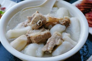 Un tazón de sopa con carne y albóndigas blancas.