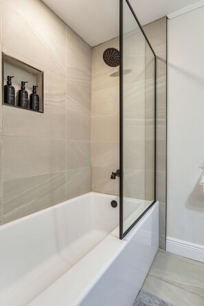Un bagno moderno con doccia vetrata, una vasca da bagno bianca e uno scaffale con articoli da toilette.