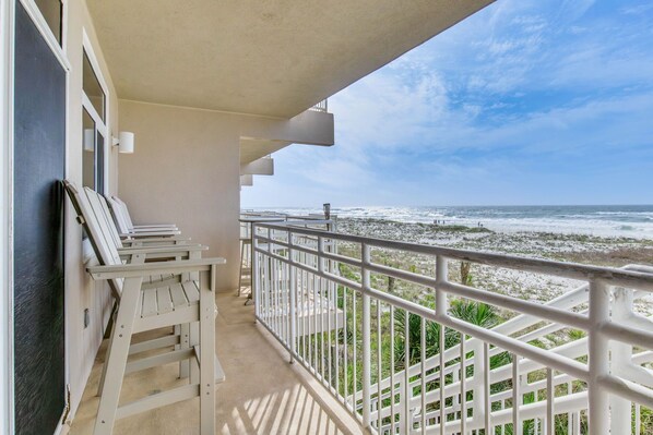 Un balcone con ringhiere bianche, vista sull'oceano e qualche sedia.