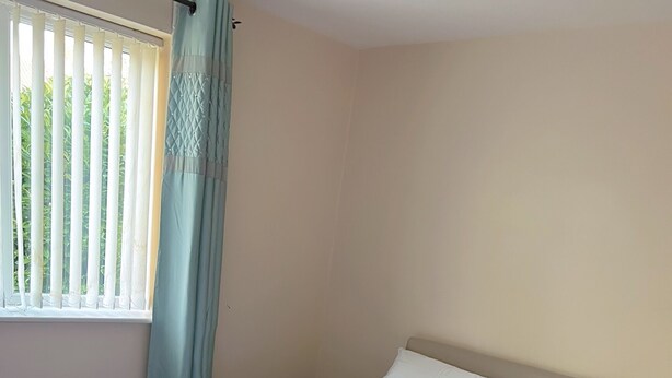 A neatly made bed with white linens and a folded towel, a window with blinds and a curtain, and a plain wall. - Lovely apartment with WiFi in charming Stretford (Stretford)