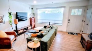 Ein Wohnzimmer mit einer Couch, einem Couchtisch, einem Fernseher und einem Fenster mit Jalousien.