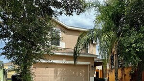 A two-story house with a beige garage door, surrounded by trees and a well-maintained lawn. - Disconnect to Reconnect! (Davenport)