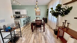 A modern kitchen with white cabinets, a dining area with a wooden table and chairs, and a large potted plant. - Disconnect to Reconnect! (Davenport)