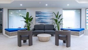 A modern lobby with a grey sofa, two armchairs, and a round coffee table. - Luxury suite pool & gym. 8 mins from Disney park (Kissimmee)