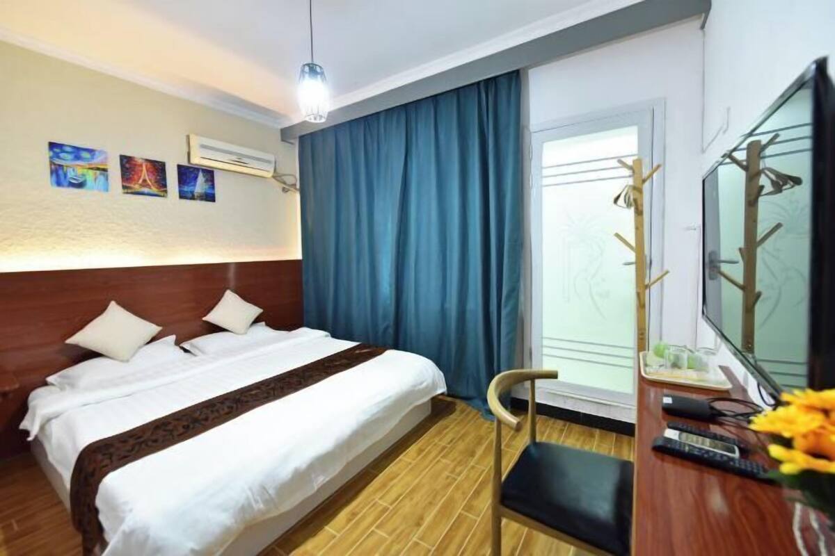 A hotel room with a bed, a desk with a chair, a TV, and a window with curtains.