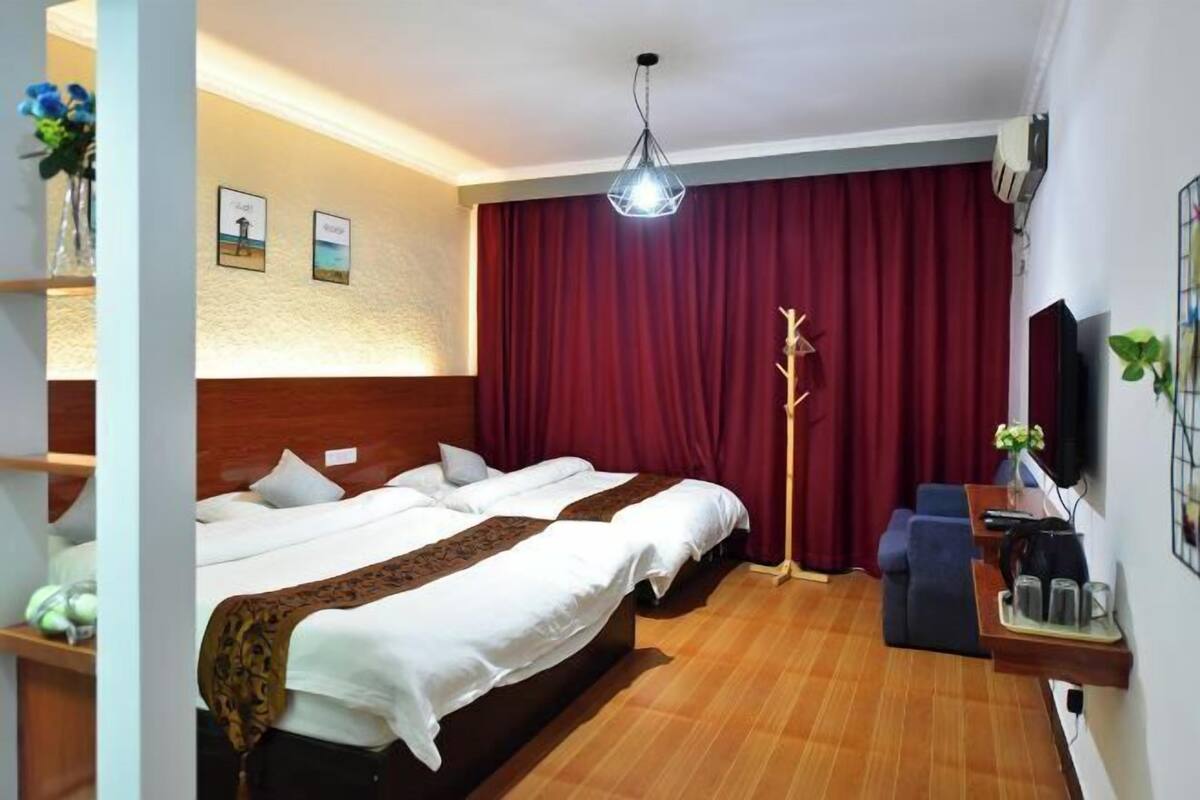 A hotel room with two beds, a desk, a chair, a television, and a red curtain.
