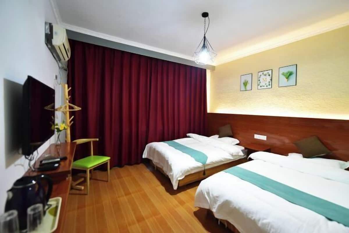 A hotel room with two beds, a desk with a chair, a TV, a ceiling light, and a red curtain.