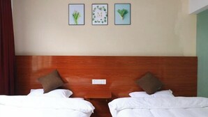 A hotel room with two beds, a wooden headboard, a small table, and three framed pictures on the wall. - Moment Inn (Huangshan City)