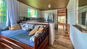Un dormitorio con cama de madera, una pequeña kitchenette y un baño visible a través de una puerta abierta.