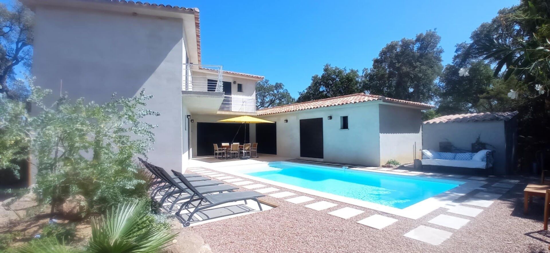 A two-story house with a swimming pool, outdoor seating, and a garden area.