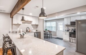A modern kitchen with a large island, stainless steel appliances, and a wooden ceiling beam. - Modern Interior, Near Downtown! Warm at Wellsville (Memphis)