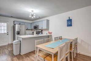 Cozinha moderna com armários azul-claros, uma geladeira de aço inoxidável, micro-ondas e pia. Há uma área de refeições com mesa e cadeiras de madeira.