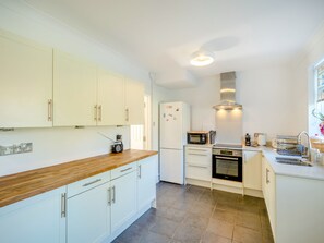 Una cocina moderna con armarios blancos, encimera de madera, microondas integrado y campana extractora de acero inoxidable.