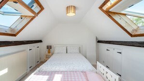 A bedroom with a sloped ceiling, skylights, a bed with a checkered bedspread, and a bedside table with a lamp. - 5 bedroom accommodation in Bransgore, near Christchurch (Bransgore, near Christchurch)