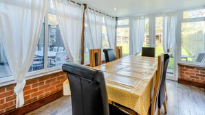 A dining area with a long table, chairs, and large windows with curtains. - 5 bedroom accommodation in Bransgore, near Christchurch (Bransgore, near Christchurch)