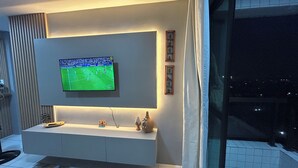 Een moderne woonkamer met een flatscreen televisie aan de muur, een witte console tafel en een vloerkleed met een patroon.