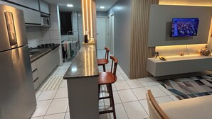 Een moderne keuken met een centraal eiland, barstoelen, een inbouwoven en een flatscreen televisie aan de muur.