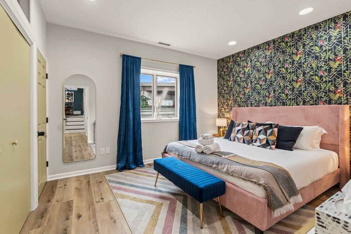 A bedroom with a bed, a bench, a mirror, and a window with curtains.