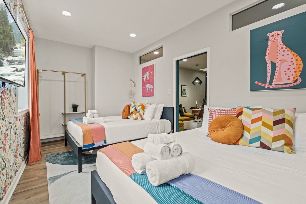 A hotel room with two beds, a shower area, and a large window with a view of a river.