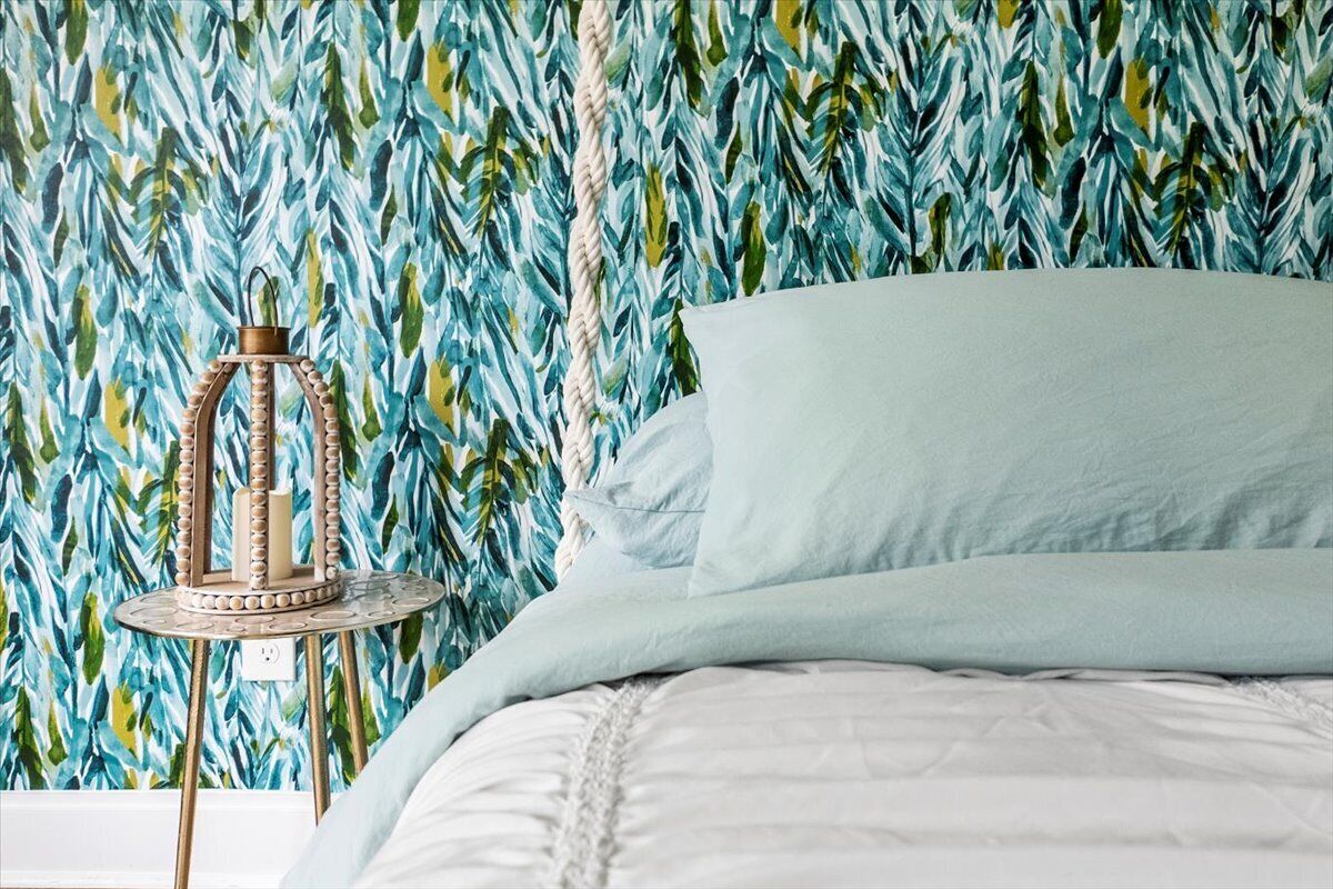Un lit avec une couette blanche et un oreiller bleu clair, adossé à un mur orné d’un motif végétal.