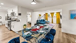 A modern kitchen with white cabinets, stainless steel appliances, and a glass dining table with blue chairs. - Spacious 4-bedroom house with AC, WiFi, Houston Hideaway 10 min to NRG (Houston)