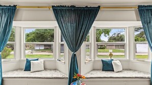 A bay window with teal curtains, cushioned seating, and a small side table with books and a vase of flowers. - Spacious 4-bedroom house with AC, WiFi, Houston Hideaway 10 min to NRG (Houston)