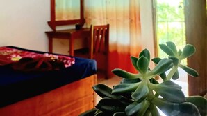 Ein Zimmer mit einem Bett, einem Sessel, einem Spiegel und einem Fenster mit Vorhängen.